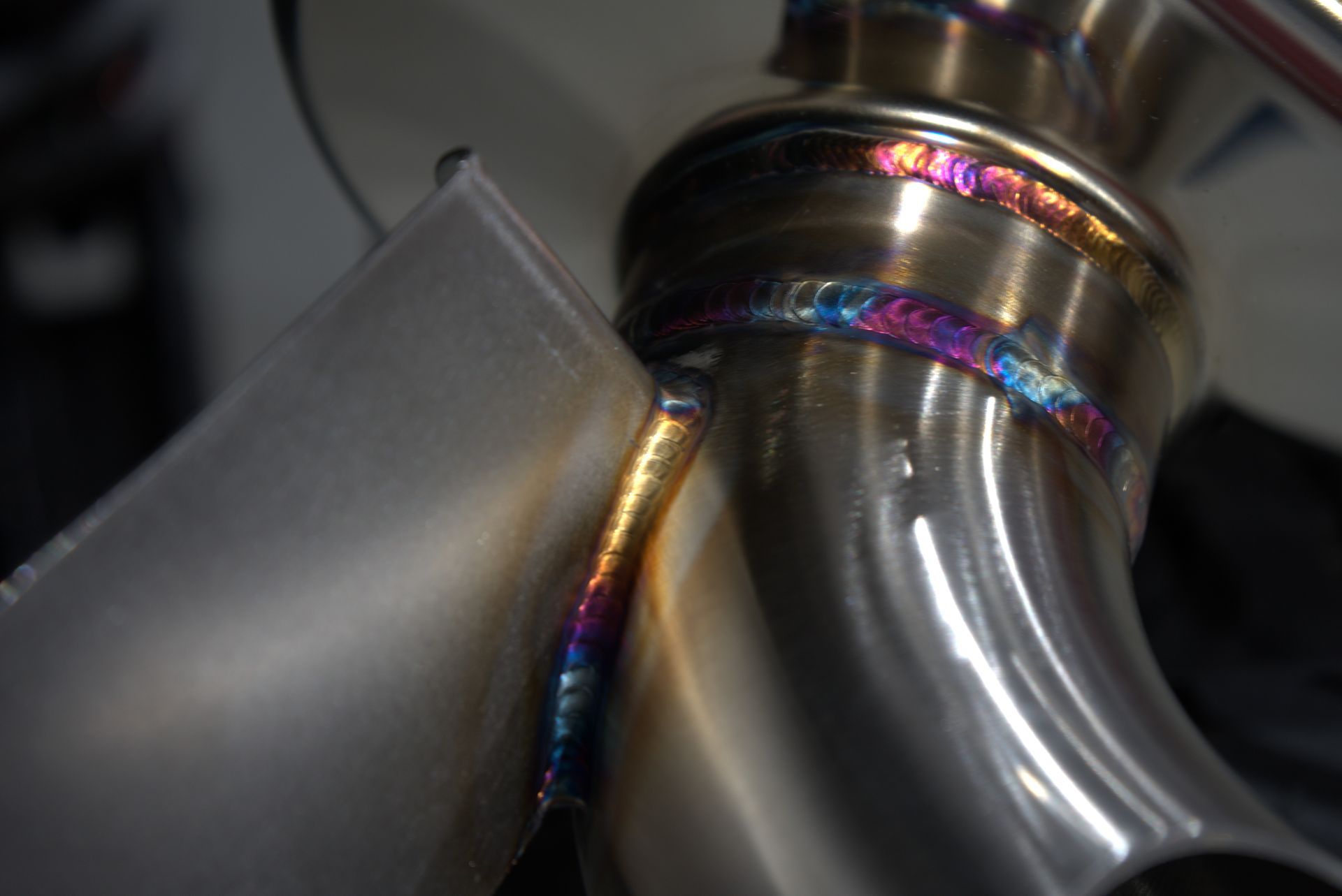 Close-up of welded metal tubes, showing iridescent weld colors: purple, blue, and gold.