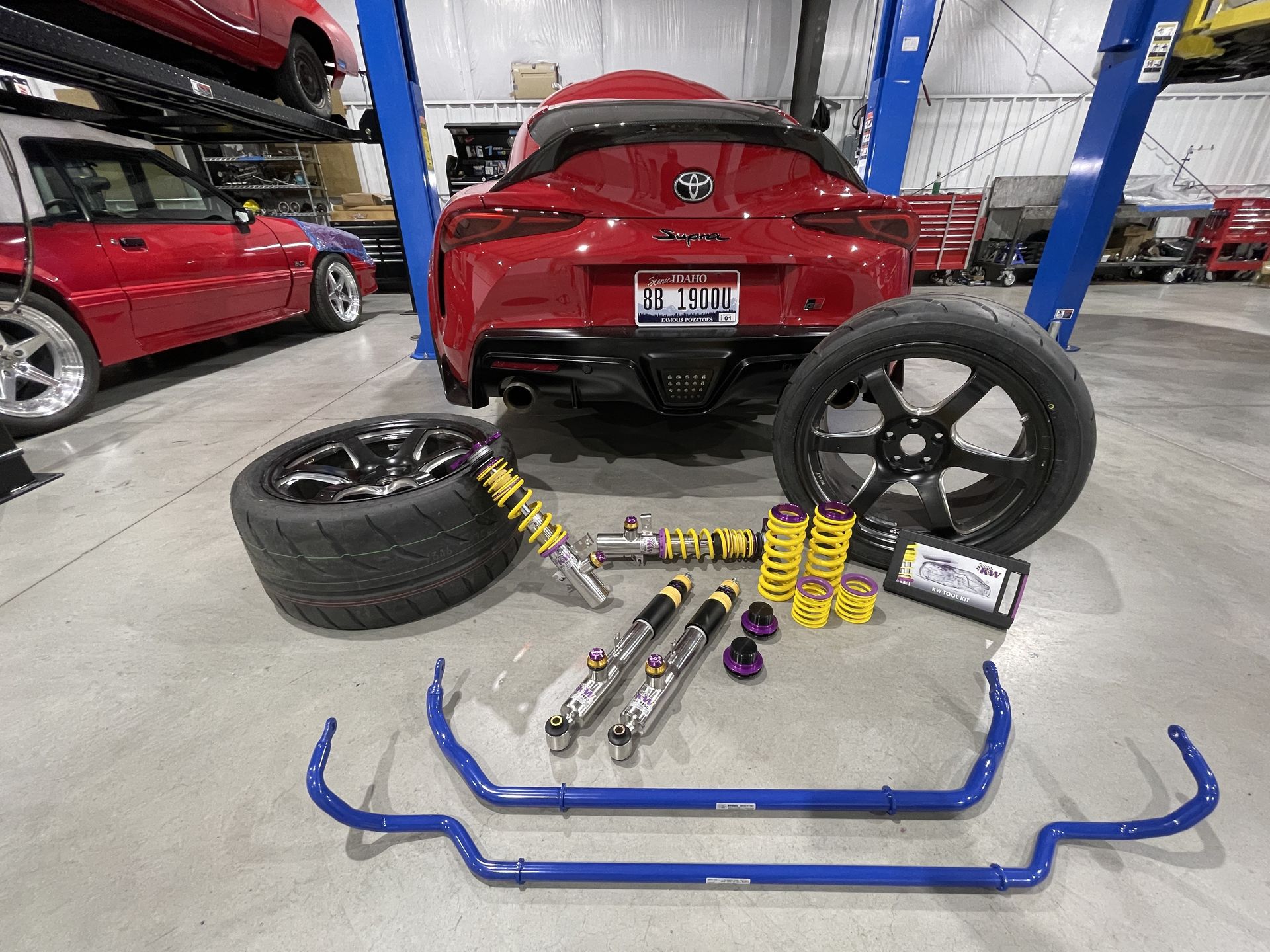Red Toyota Supra with aftermarket suspension parts, wheels, and sway bars in a garage.