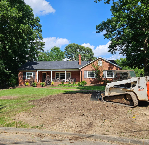 Red brick house with a lawn being worked on by a skid steer under a blue sky.