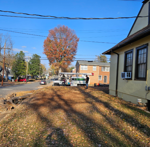 Street scene: tree with fall foliage, parked service vehicle, person near vehicle, brick building and house on sunny day.