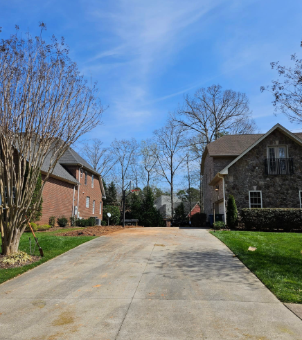 Driveway leading to brick houses under a blue sky, with bare trees and green grass.