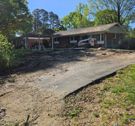 A brick house undergoing landscaping, with a skid steer in the front yard and a paved driveway.