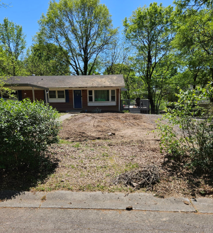 House with cleared front yard; dirt and remnants of plants on ground; sunny day.