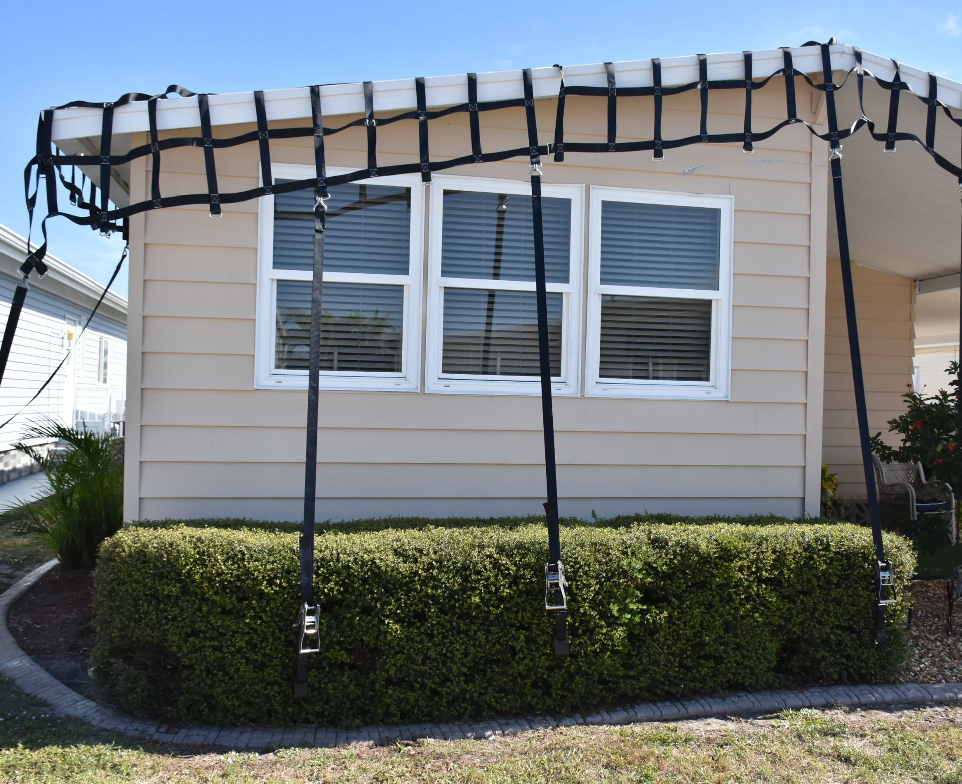 Tan house with a net canopy over a window and a hedge below. Black straps support the net structure.
