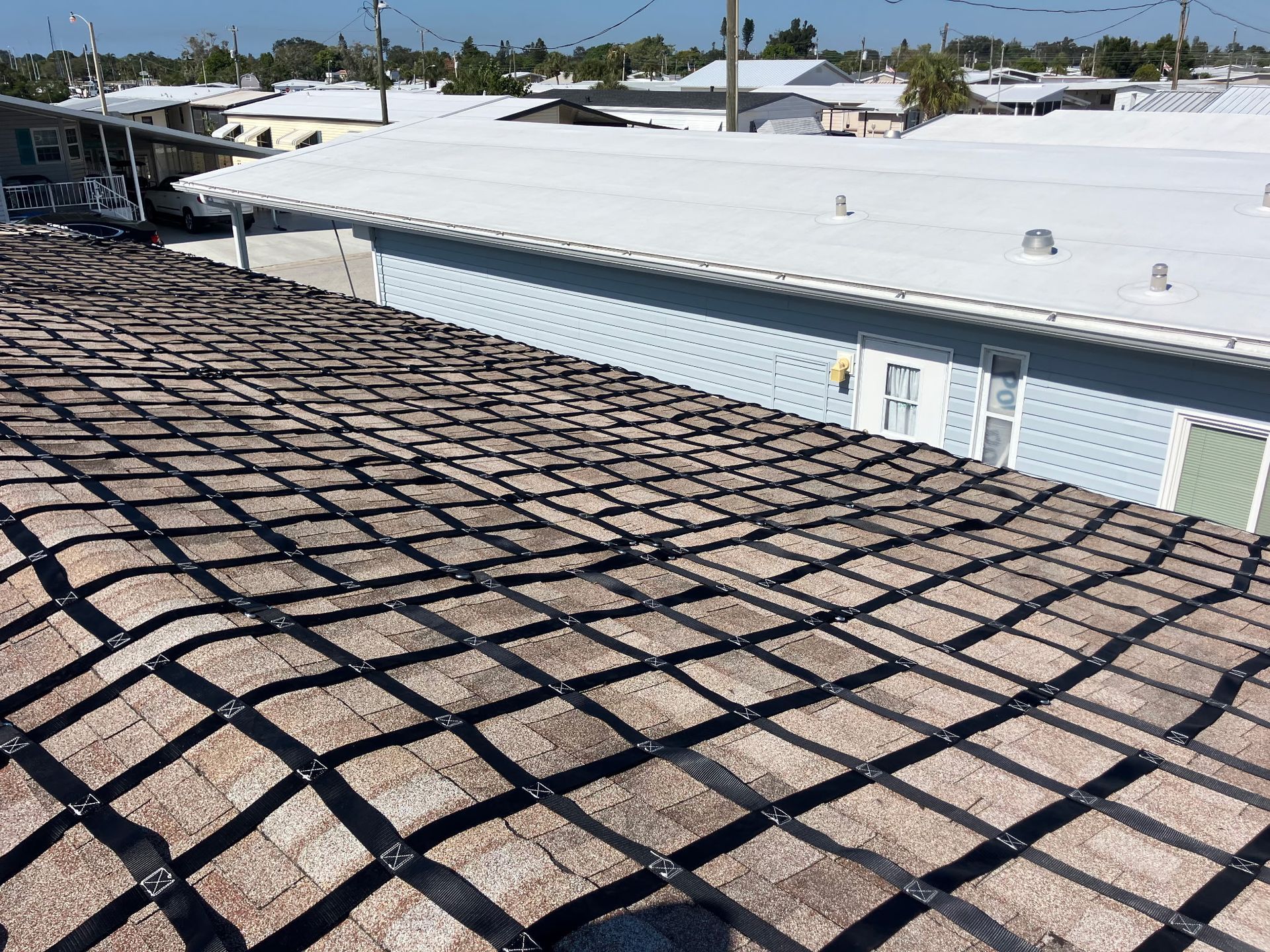 Brown shingle roof with black grid system, overlooking a neighborhood with white and blue buildings.