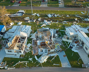 Aerial view: Homes damaged by hurricane, debris scattered across lawns, residential area.