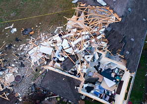 Aerial view of a house destroyed by a disaster, scattered debris, damaged roof, wood and possessions strewn.