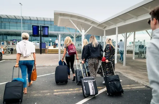 Travelers pulling rolling suitcases outside an airport terminal