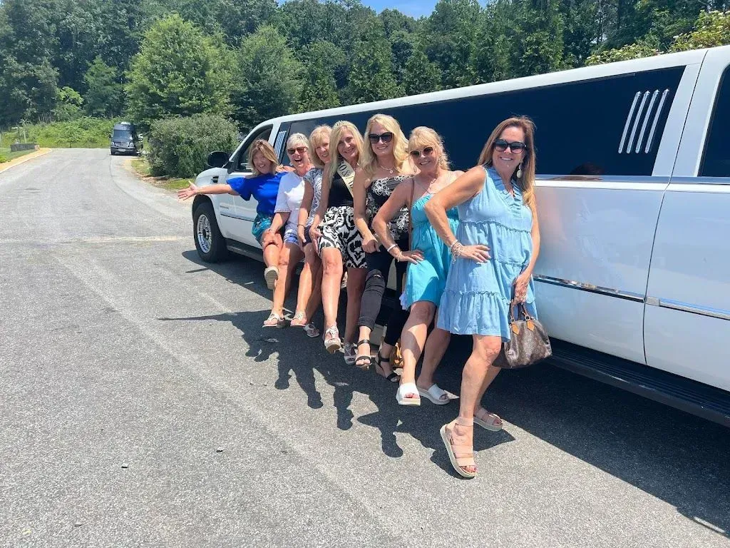Six people leaning from a white limousine parked on a sunny roadside, smiling