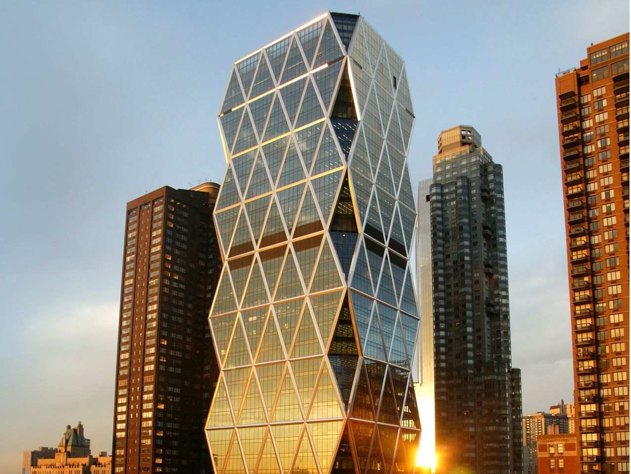 A tall building with a diamond shaped facade is surrounded by other tall buildings