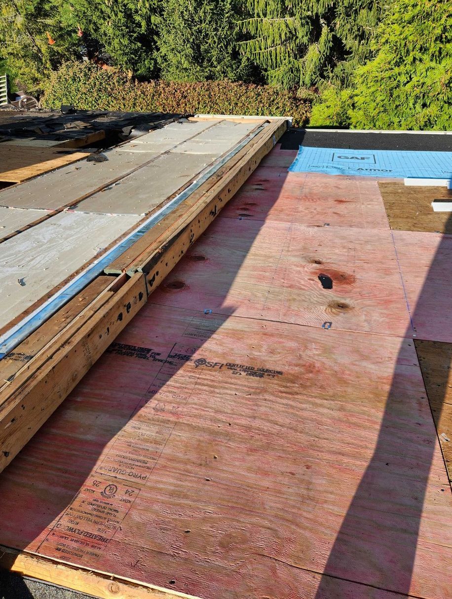 A construction site showing a roof under repair with exposed plywood sheathing and a raised wooden structural beam.