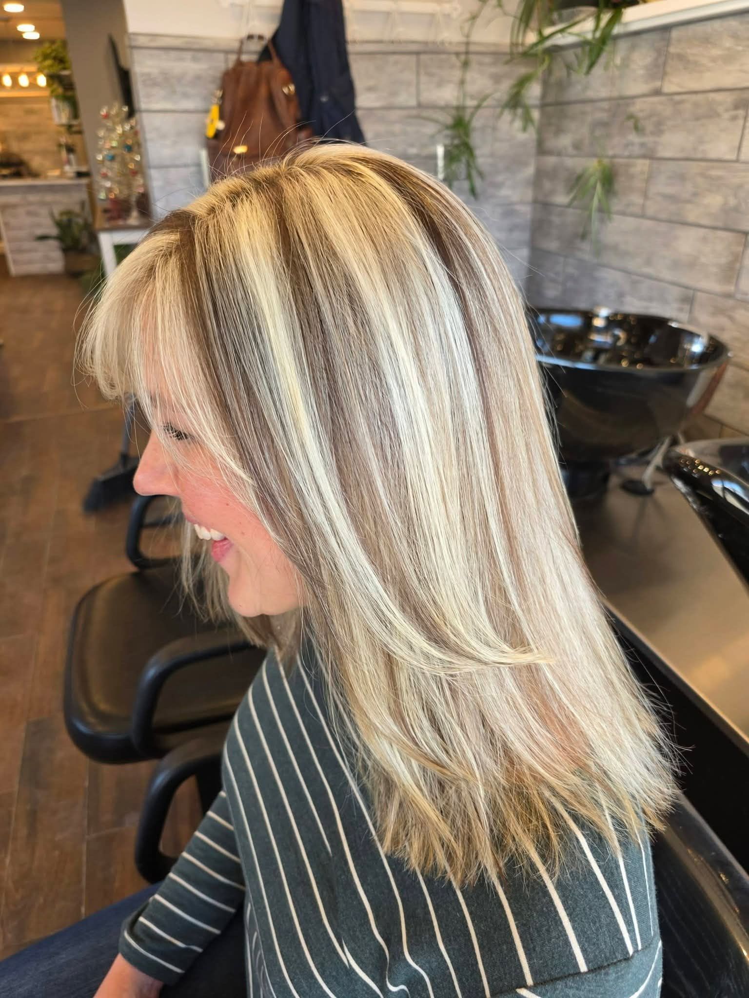 Woman with blonde and brown striped hair, smiling, in a salon chair.