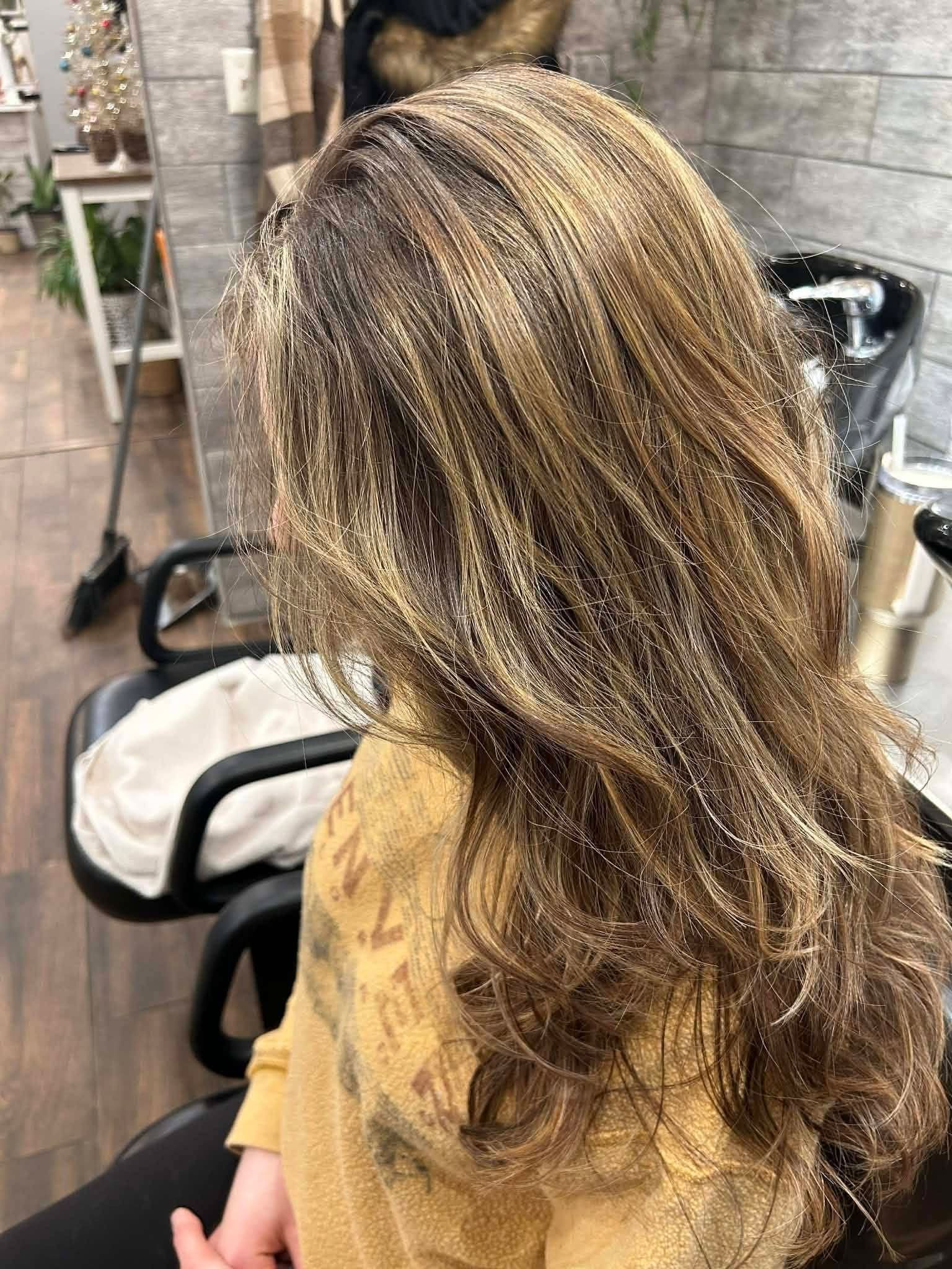 Person with layered brown hair, gold highlights, seated in a salon chair.