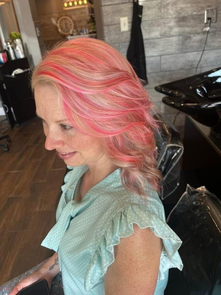 Woman with pink and blonde hair in a salon chair, wearing a light blue top.
