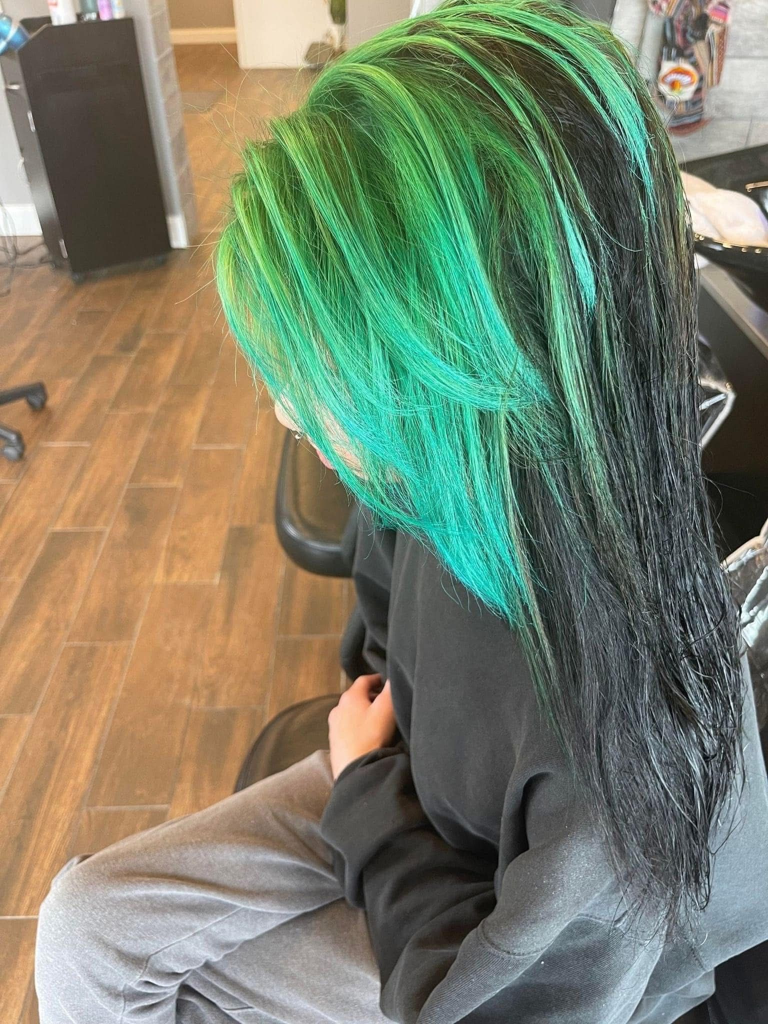 Person with green and black braided hair, sitting in a salon chair.