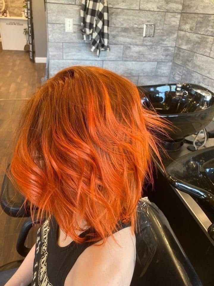 Woman with vibrant orange hair in a salon chair, near a sink.