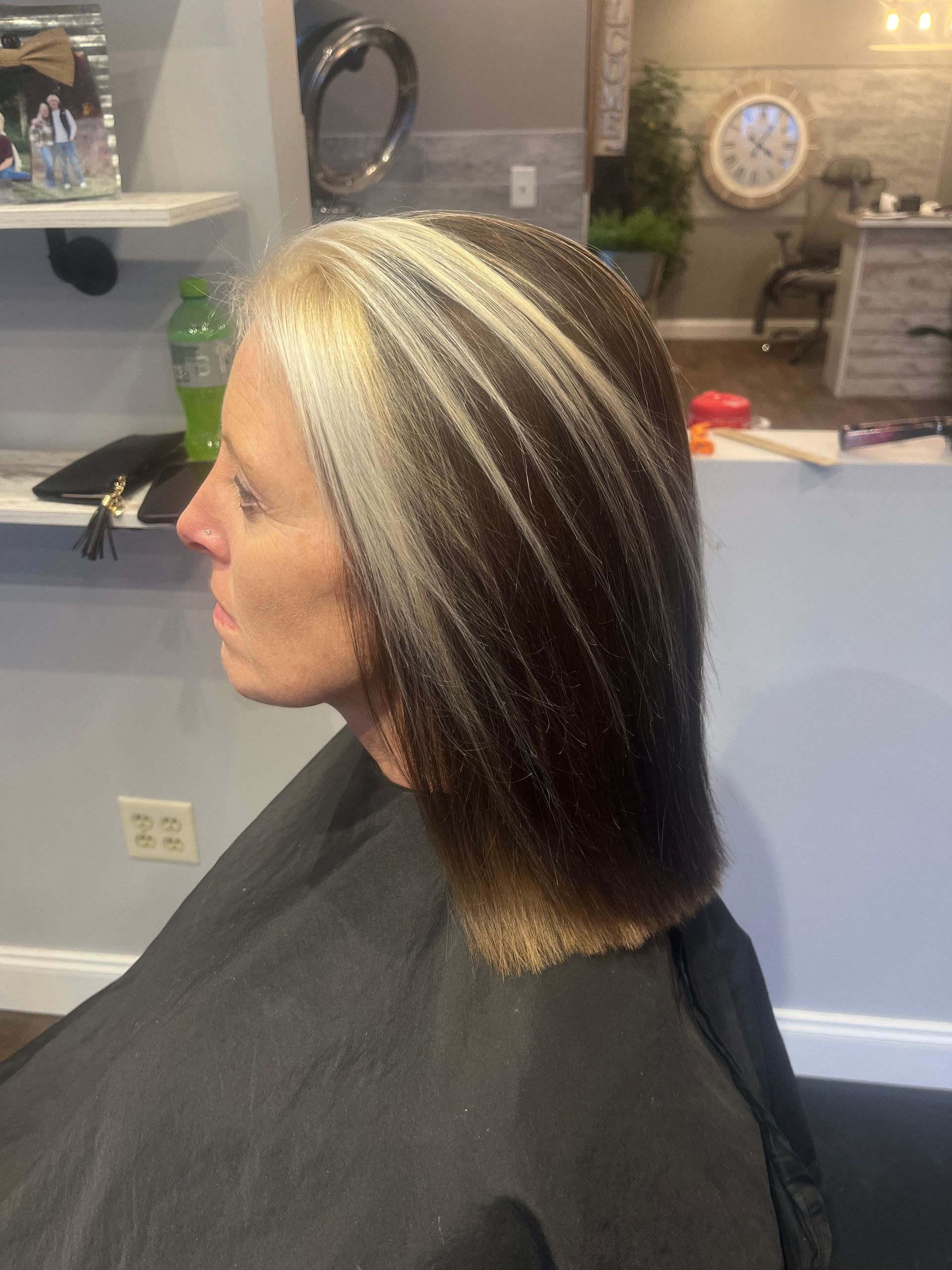 Woman's hair colored with a bright blonde streak in front, brown elsewhere. She is in a salon chair.