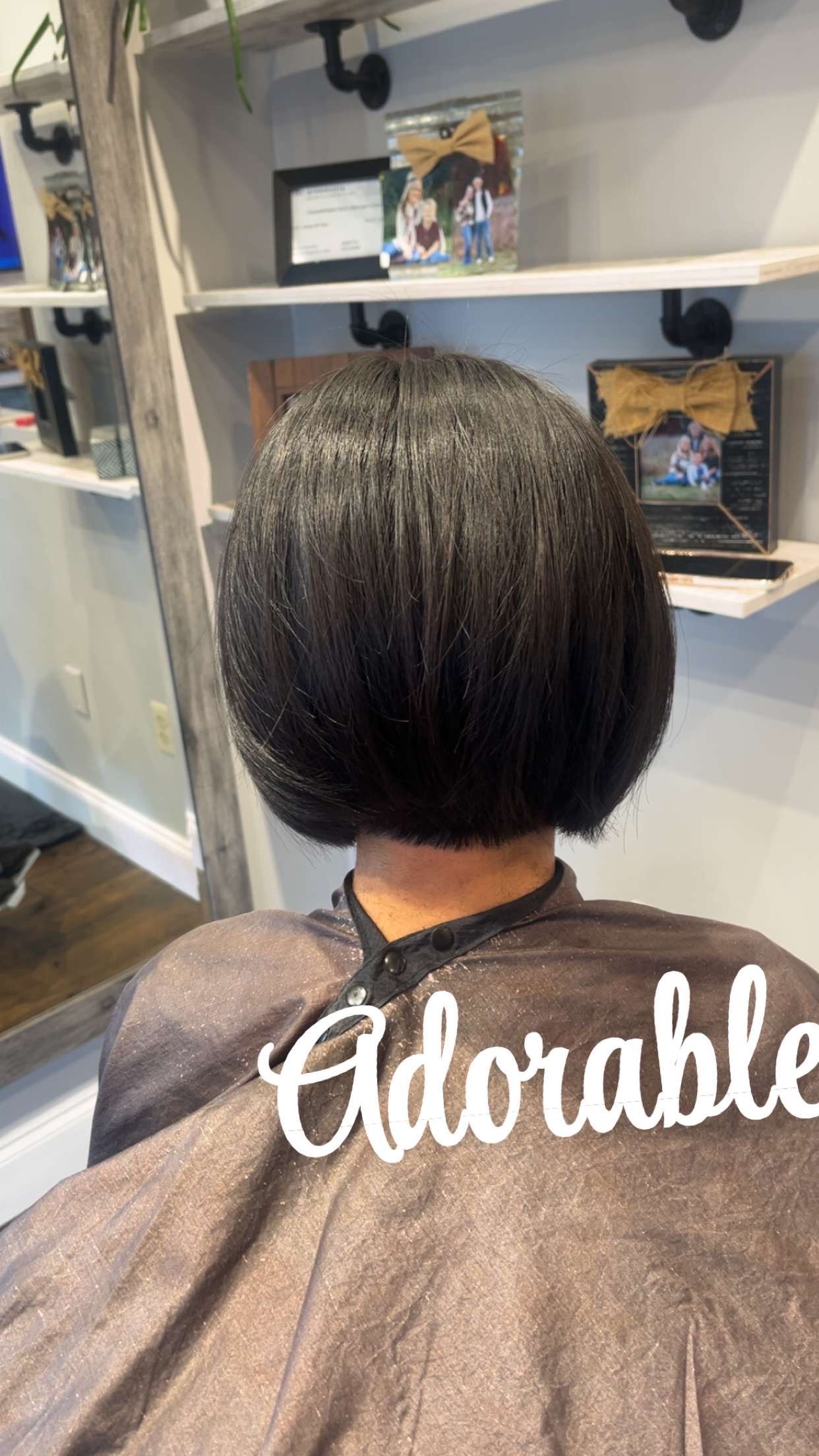 A person with a bob haircut wearing a salon cape; “Adorable” sign. 