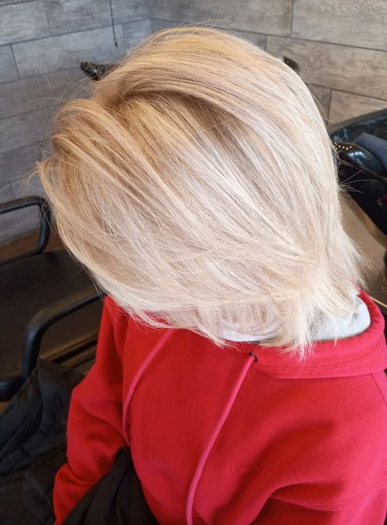Blonde layered bob haircut, red sweatshirt, indoor salon setting. 
