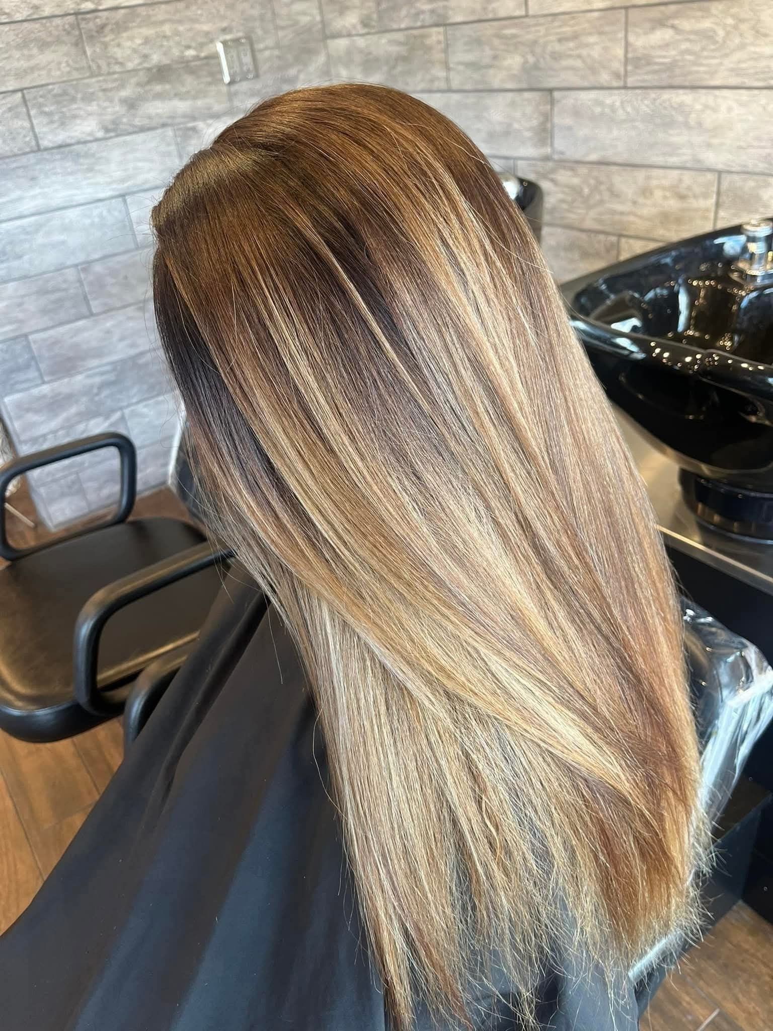 Woman's hair, a mix of brown and blonde highlights, styled straight in a salon setting. 