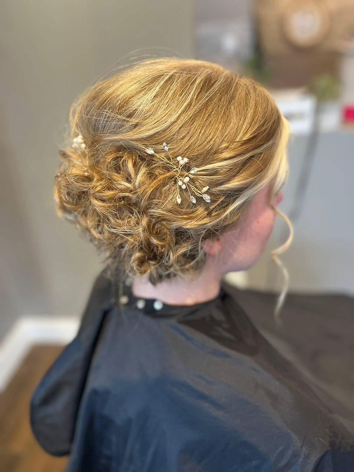 Updo hairstyle with loose curls and decorative hairpins; salon setting.