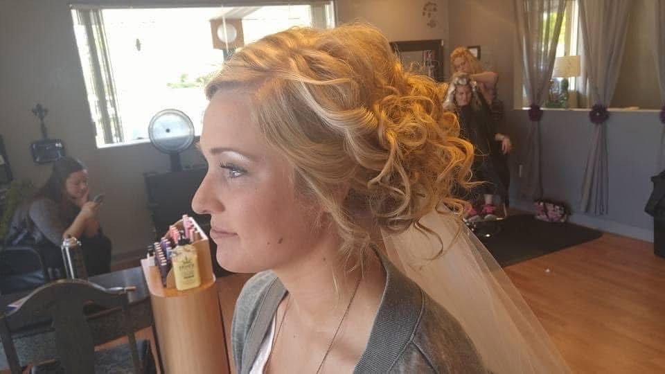 Woman with blonde curly updo and veil, wearing a gray sweater, indoors.