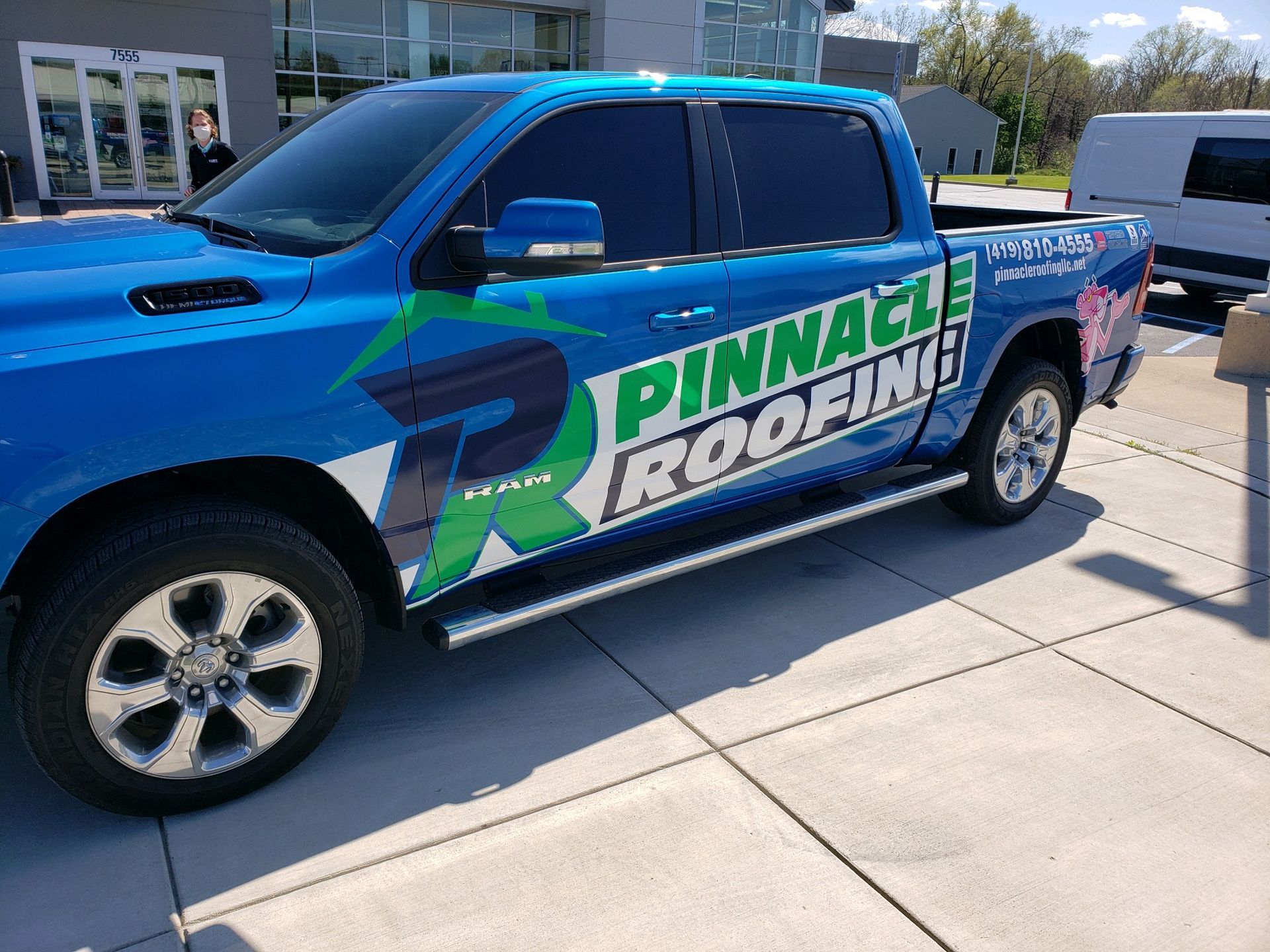 A blue Pinnacle Roofing pickup truck parked in a paved lot on a sunny day.