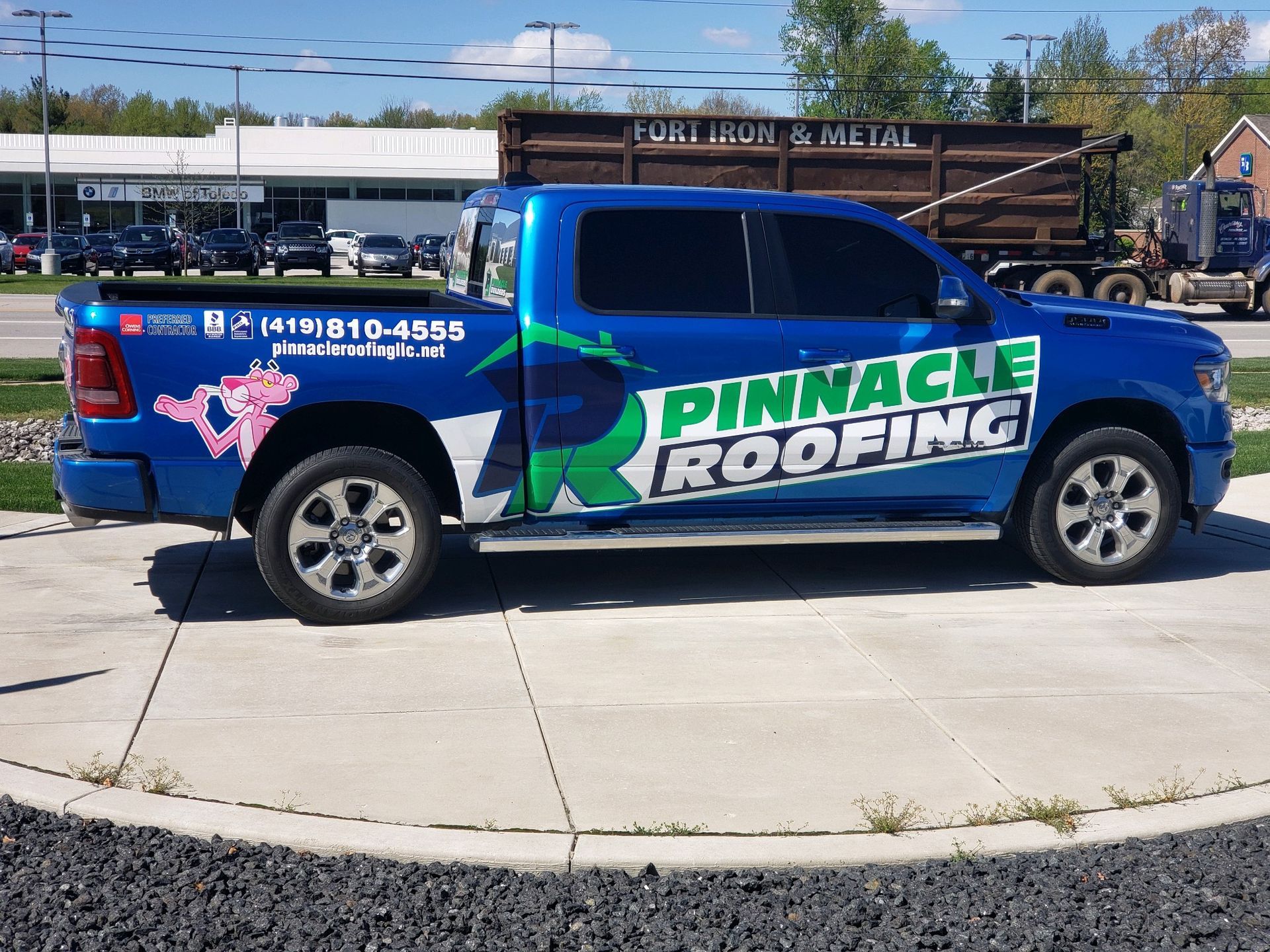 A blue Pinnacle Roofing pickup truck featuring a pink panther graphic parked in an outdoor lot.