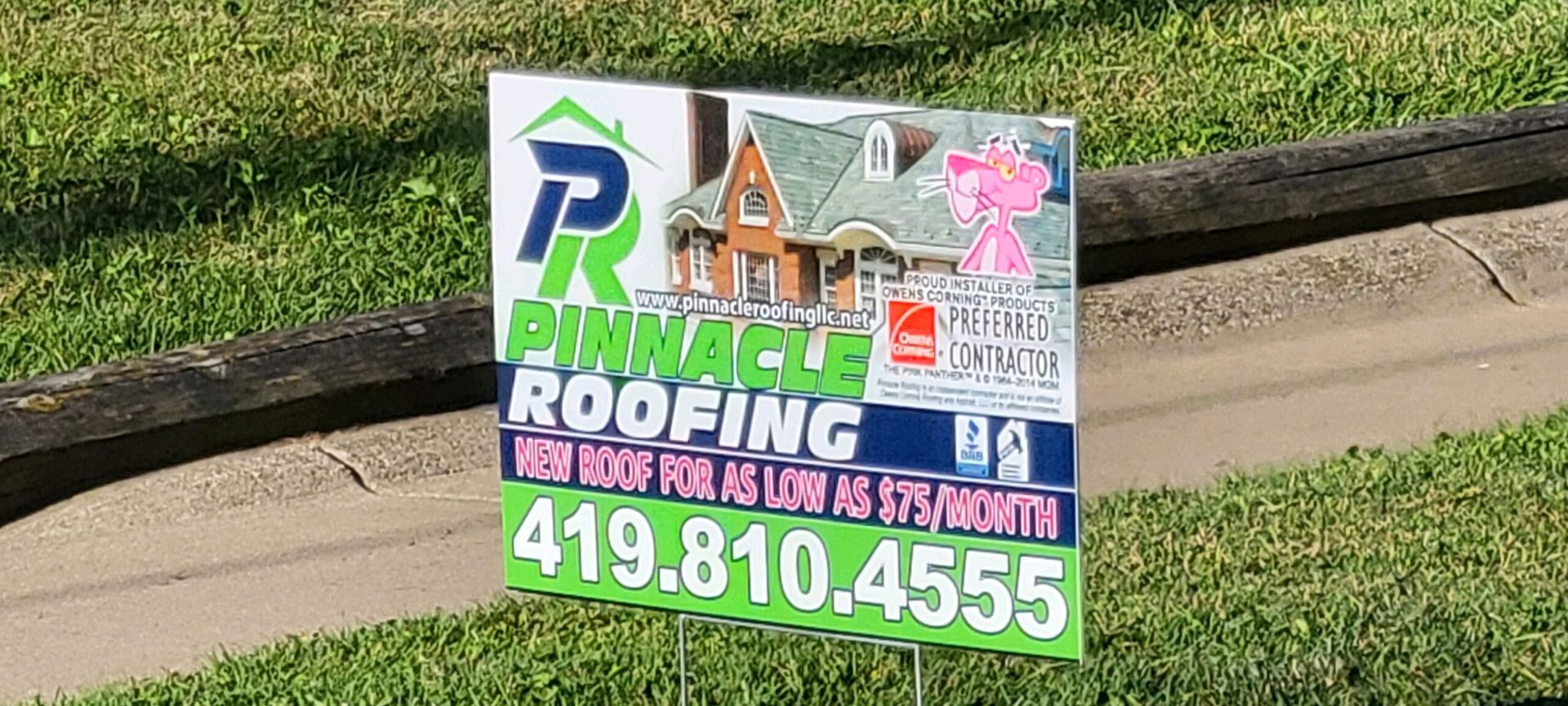 A Pinnacle Roofing yard sign with a house image, pink panther cartoon, and phone number 419-810-4555 on a lawn.