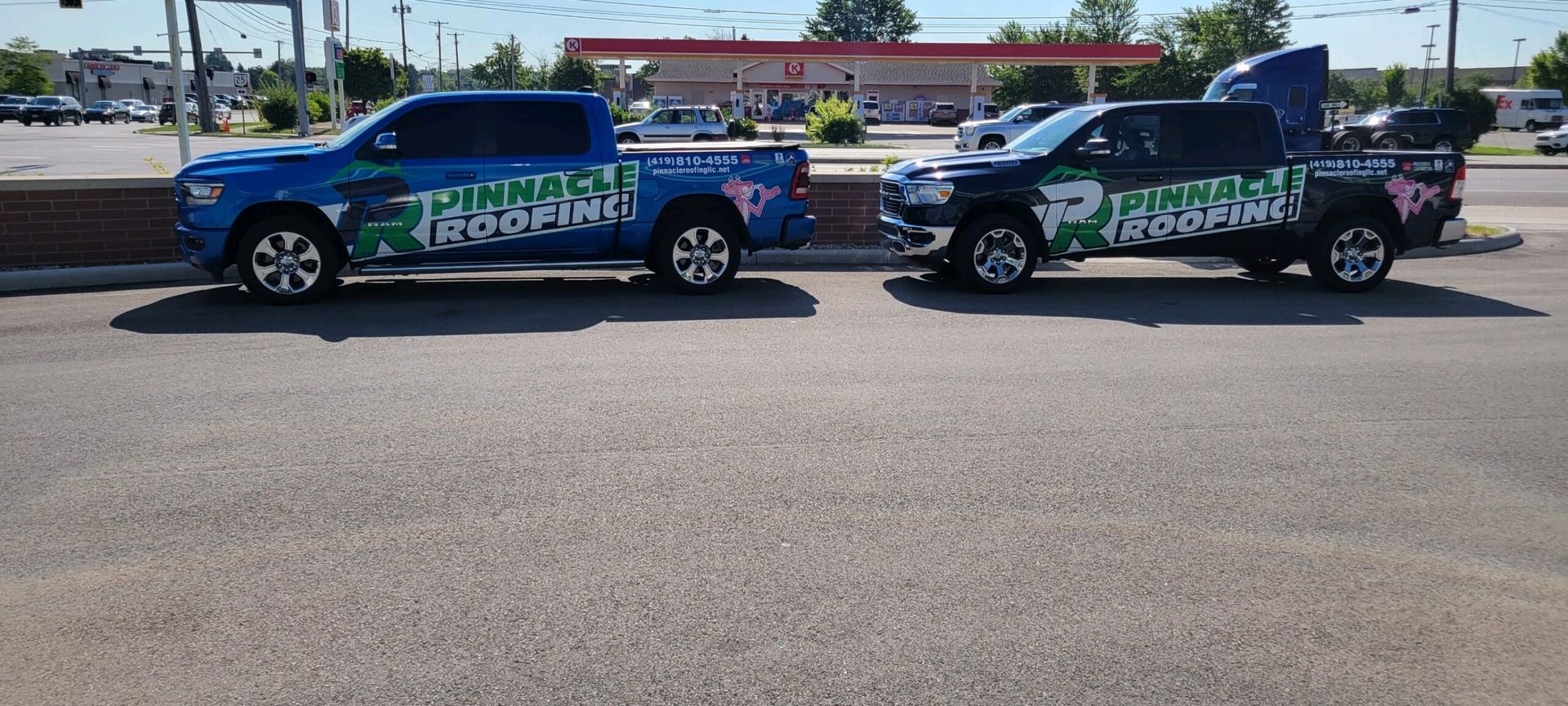 Two branded pickup trucks parked side-by-side in a parking lot near a gas station.