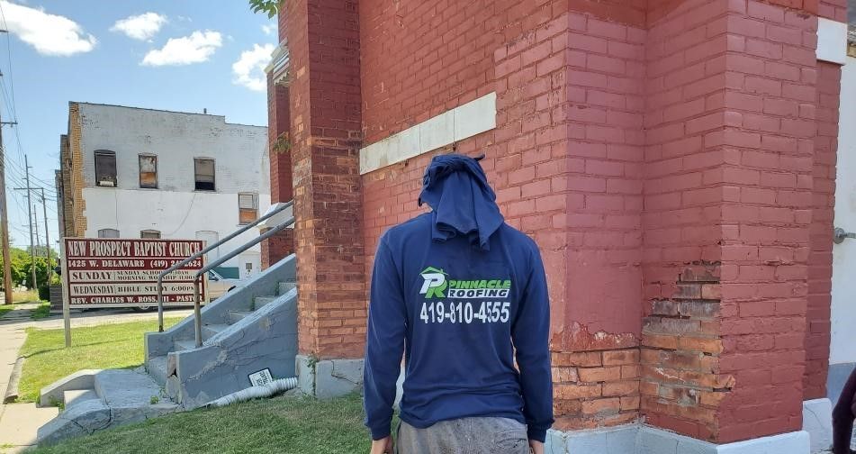 A person in a blue long-sleeved shirt stands before a weathered red brick building with an outdoor sign.