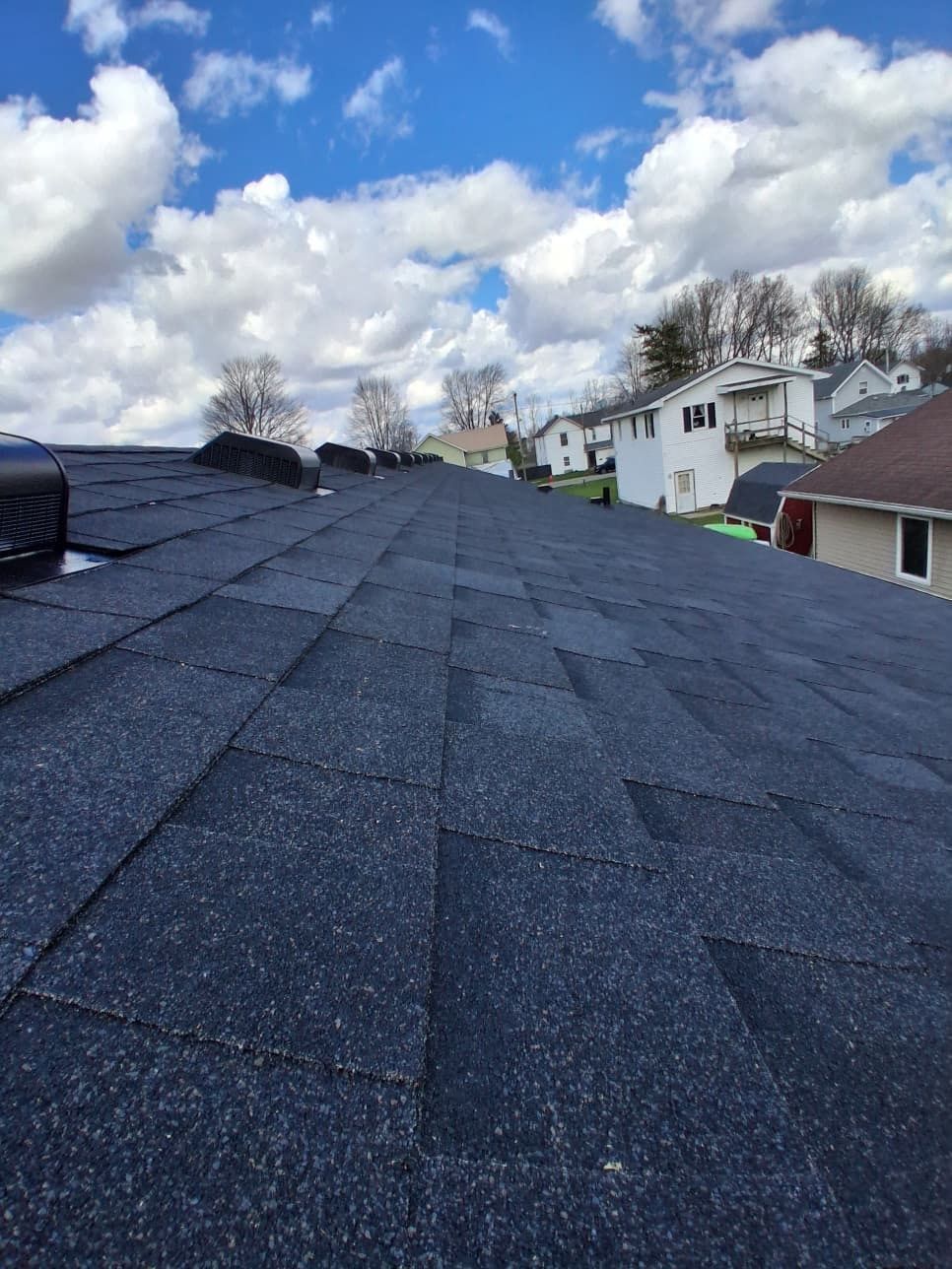 Dark shingle roof under a partly cloudy sky, with houses visible in the distance.