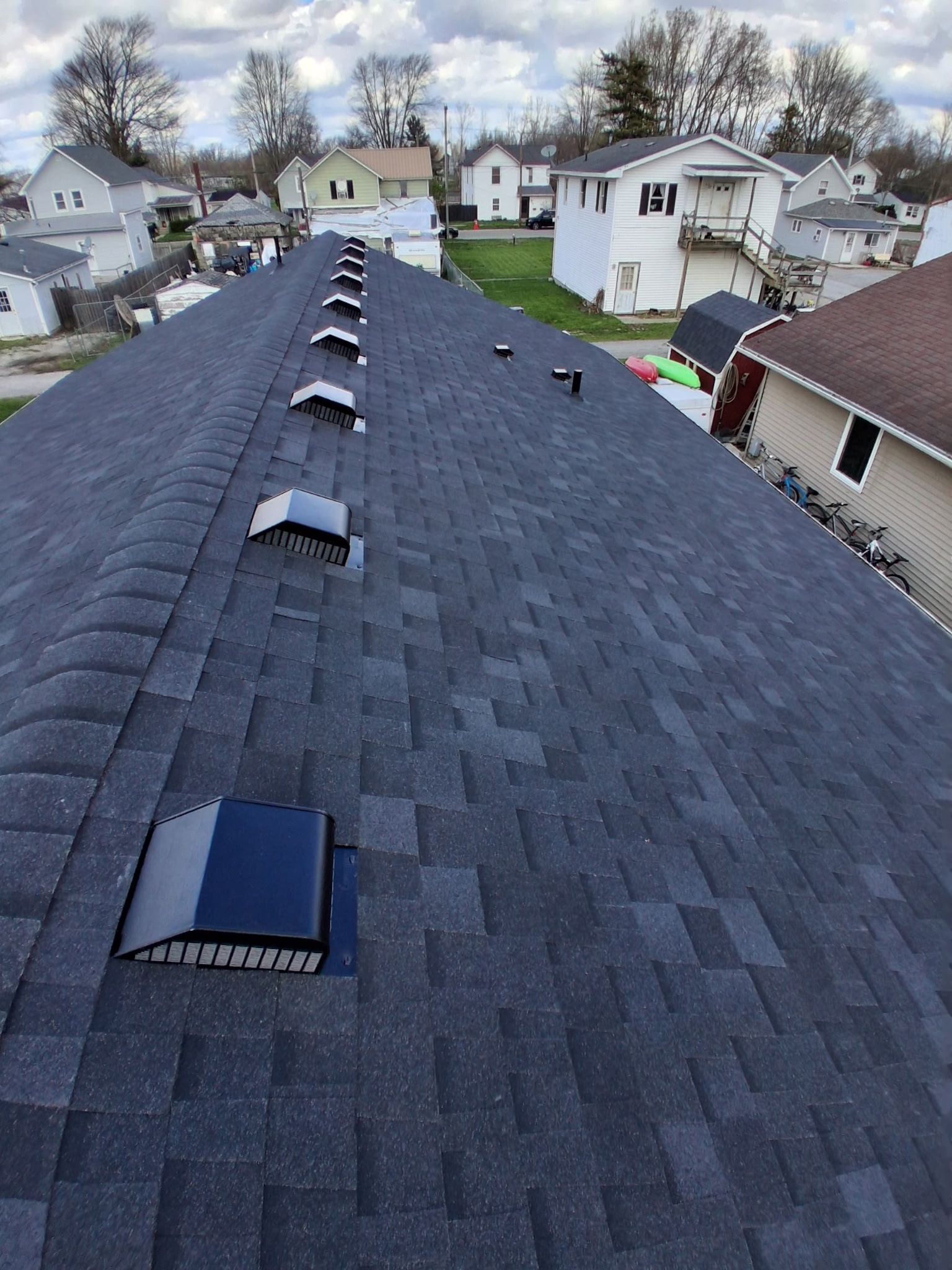 Rooftop with dark shingles and vents in a suburban neighborhood under cloudy skies
