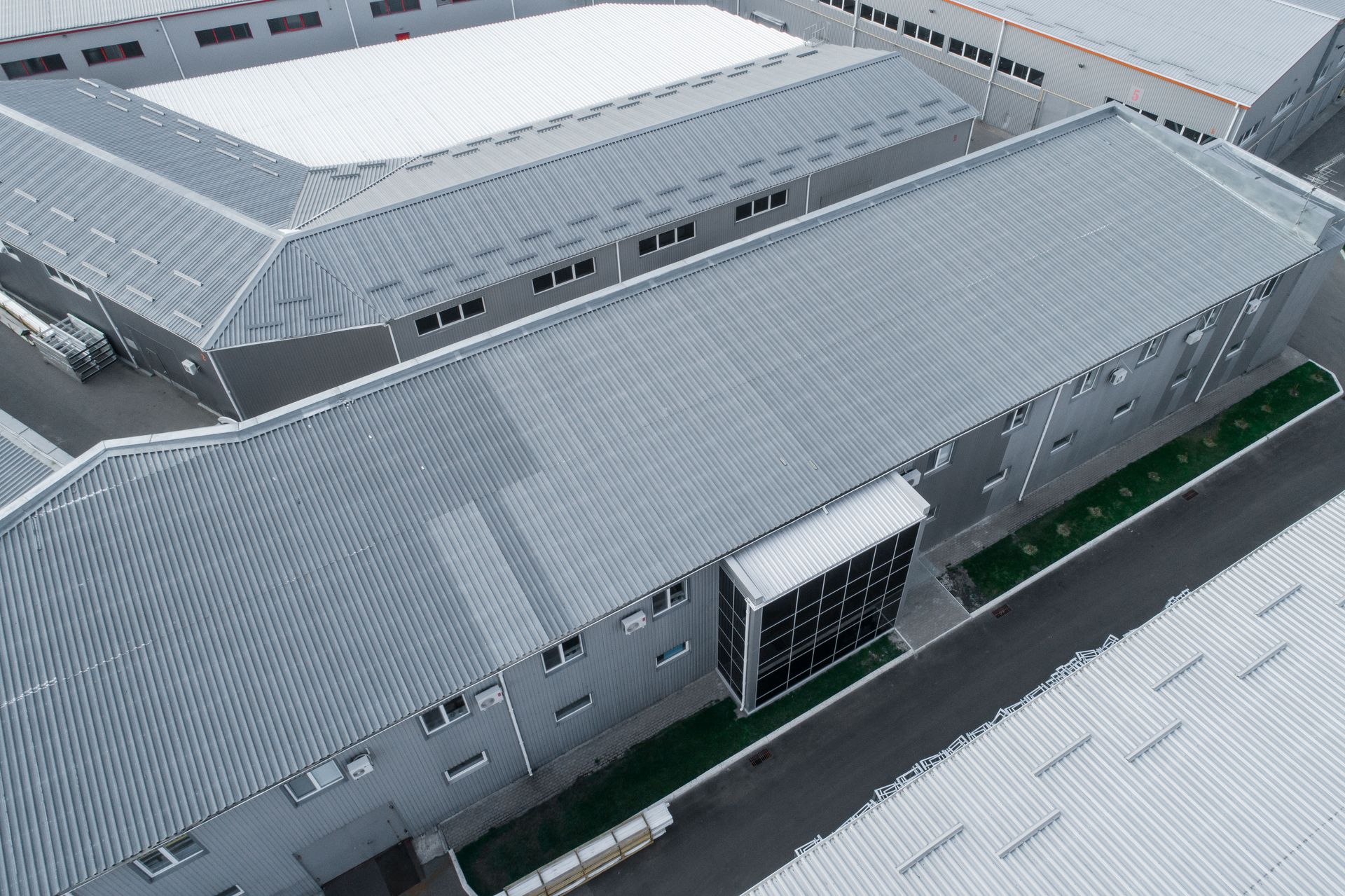 An aerial view of gray industrial warehouse buildings with metal roofs and a small section of office windows.