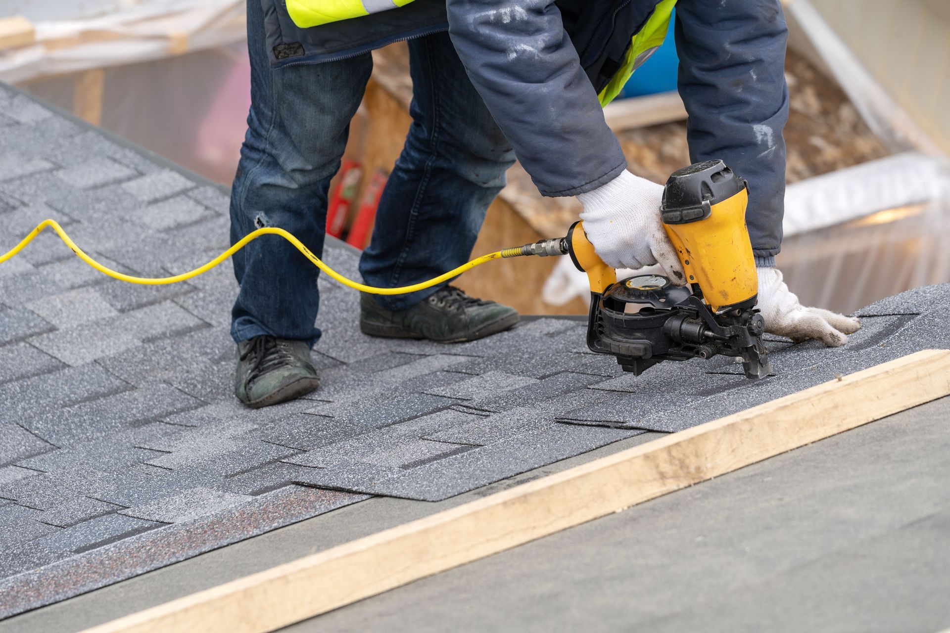A roofer uses a pneumatic nail gun to attach asphalt shingles to a roof.
