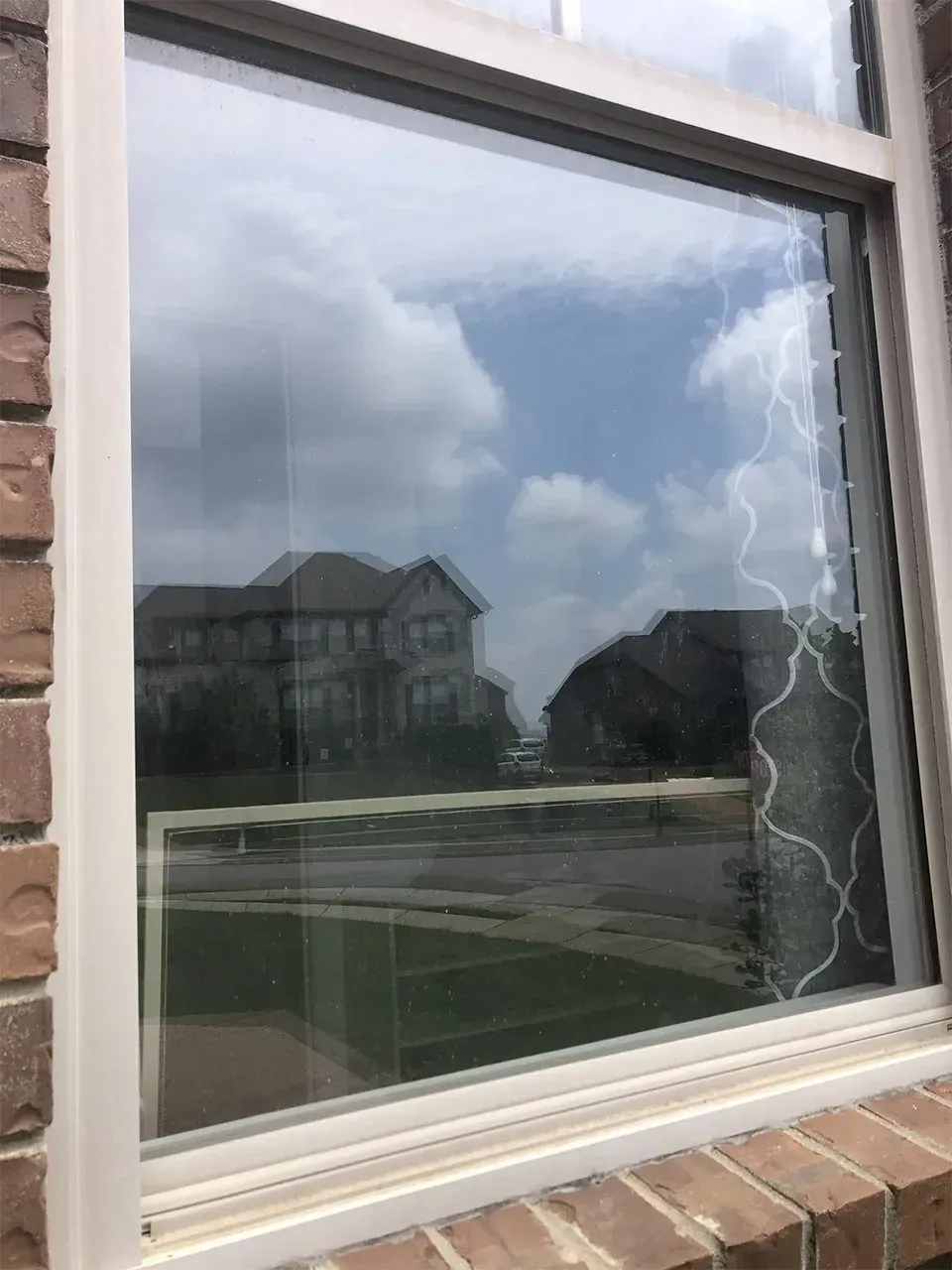 Window reflecting sky, clouds, and houses on a sunny day, with a gray curtain visible.