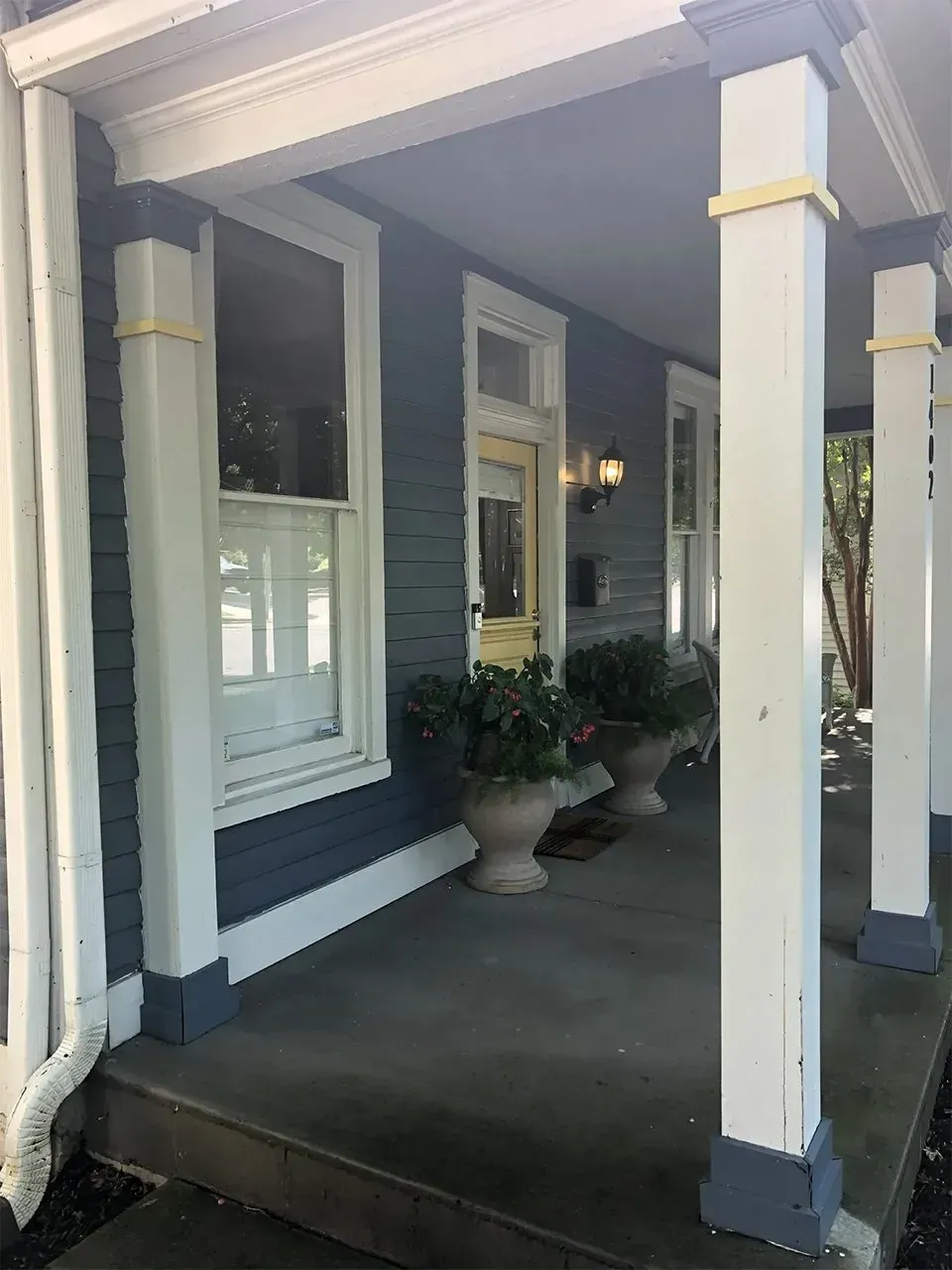 Blue house with white columns, porch, two windows, and planters.