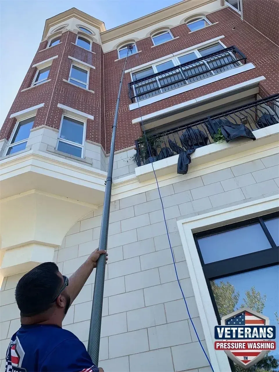 Man cleaning windows of a brick building with an extended pole. Sunny day.