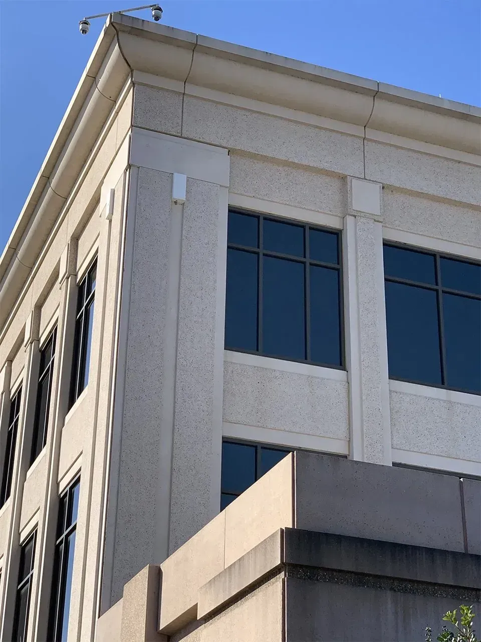 Beige building corner with dark windows, clear sky. Security cameras on top.