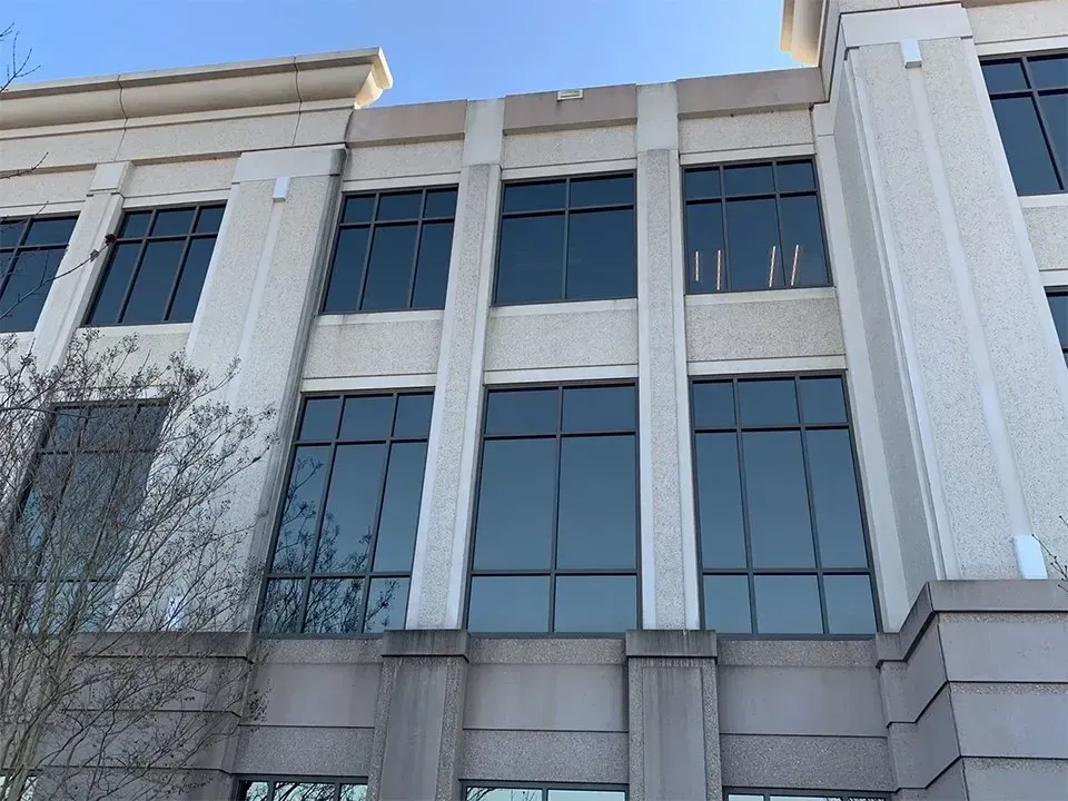 Exterior of a beige multi-story building with large windows reflecting the sky; sunny day.
