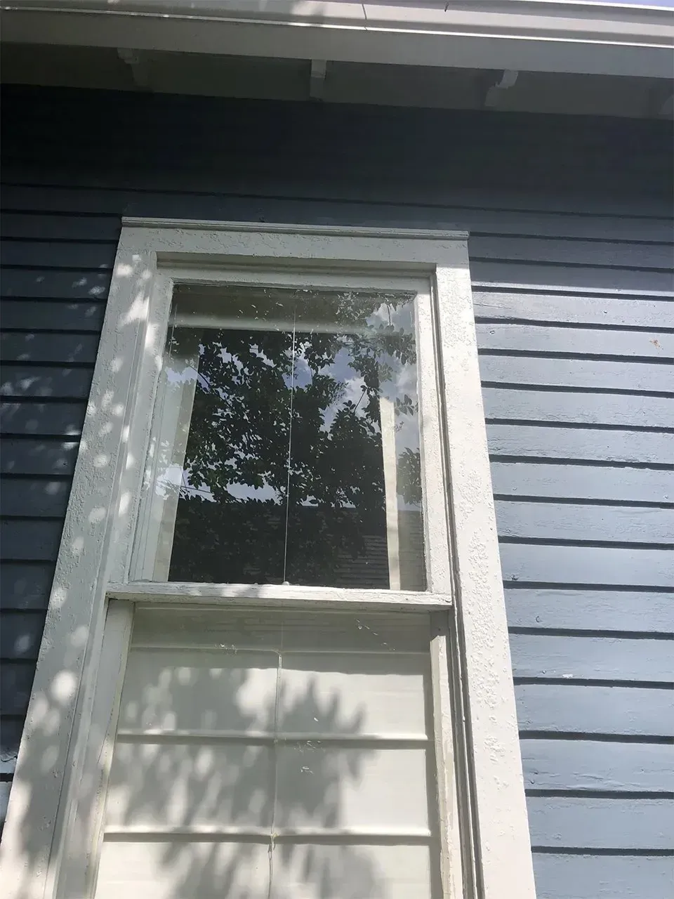 White framed window on a blue clapboard house. Sunlight reflects in the glass.