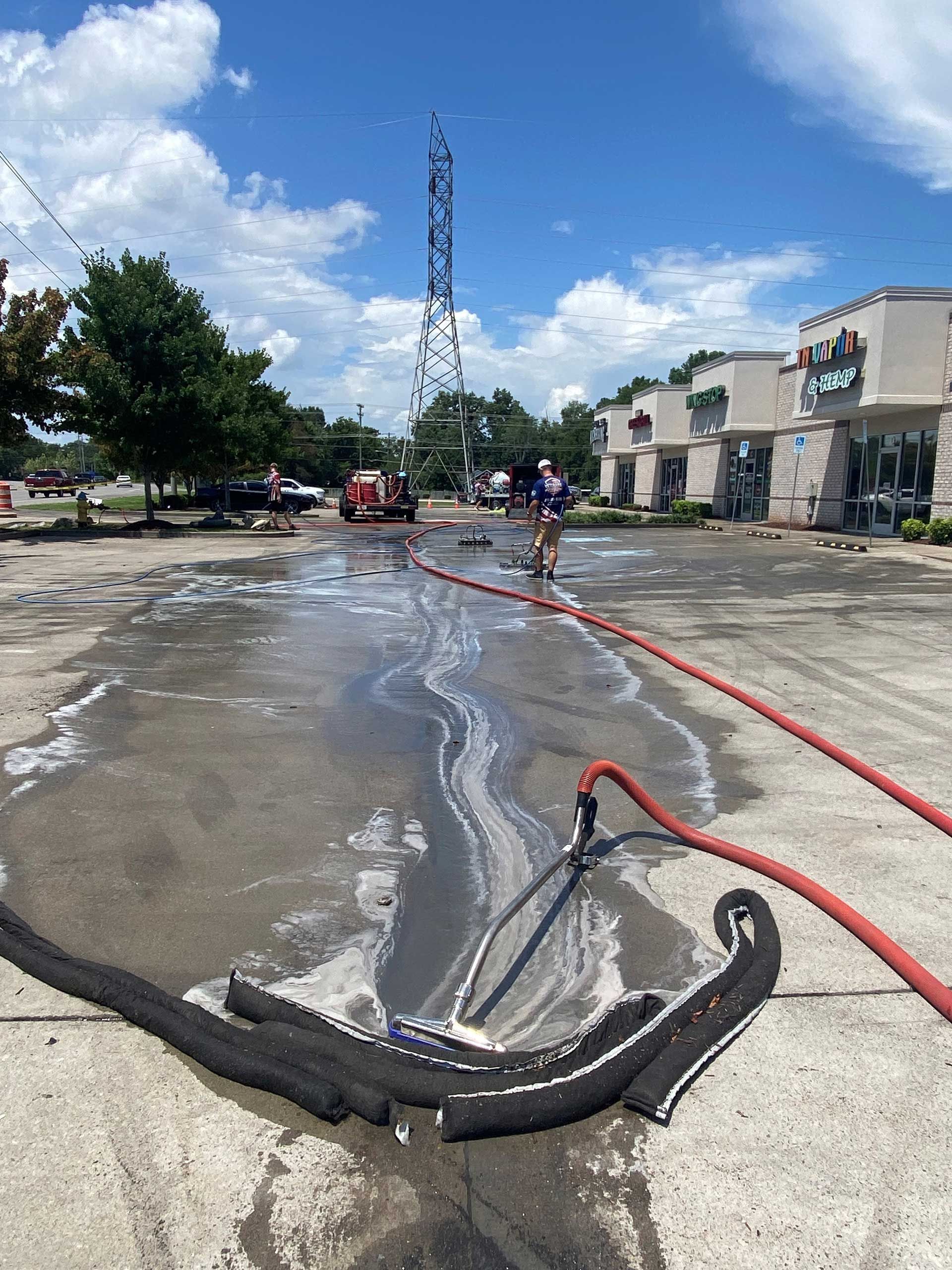 Firefighters clean up spill with hose; parking lot; tall utility tower.