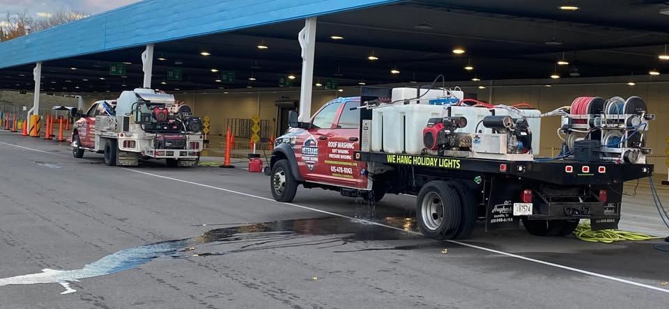 Two trucks parked under a blue awning, likely for cleaning or maintenance. Orange cones and equipment visible.