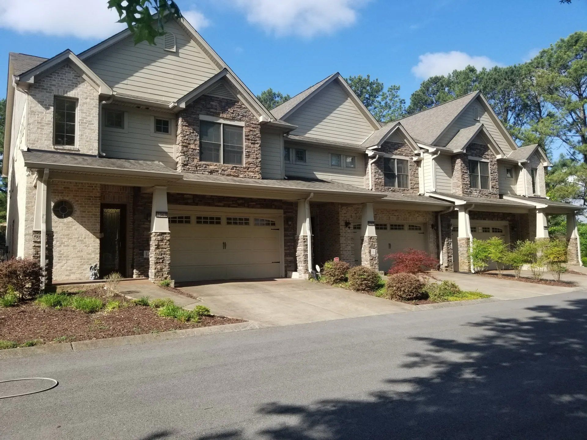 Townhomes with tan stucco, stone accents, and attached garages on a sunny day.