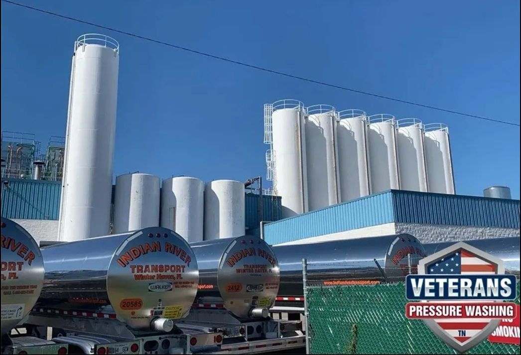 Large industrial facility with silos and tanker trucks. Clear blue sky. 