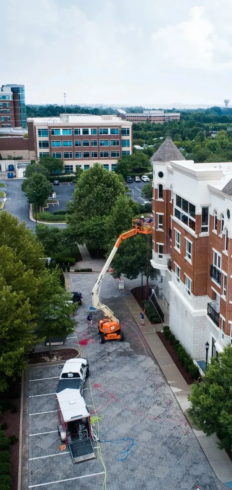An aerial view of an apartment building with a boom lift assisting with work; parked cars and trees are also visible.
