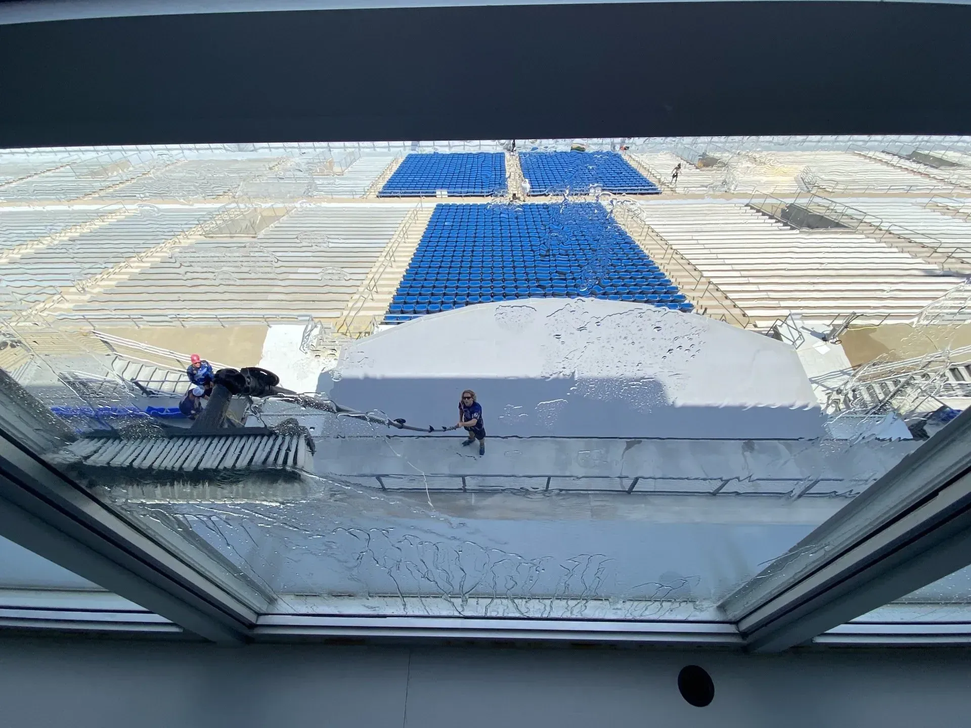Person cleaning windows on a building rooftop overlooking blue stadium seats.