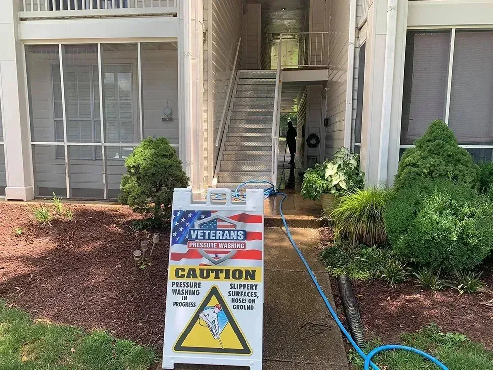 Sign warns of slippery surfaces as a veteran's group pressure washes stairs outside an apartment building.