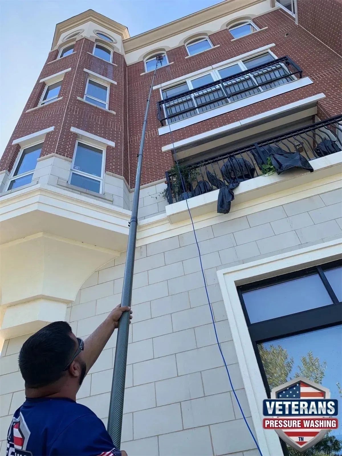 A man washes windows on a brick building with a long-handled tool.