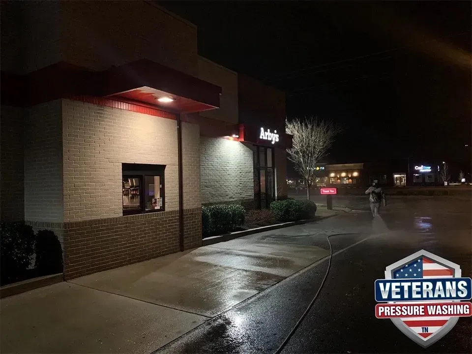 A person pressure washing the sidewalk in front of an Arby's restaurant at night.